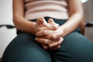 foto das mãos de uma mulher, sentada, apertando os dedos com força e o polegar pressionando o outro